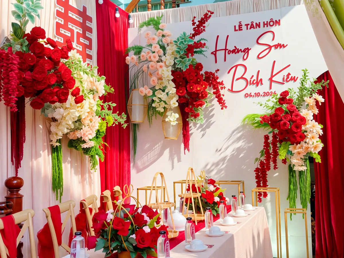 Trang trí lễ tân hôn tại nhà với phông trắng, rèm đỏ, chữ hỷ và các cụm hoa lụa đỏ, kem