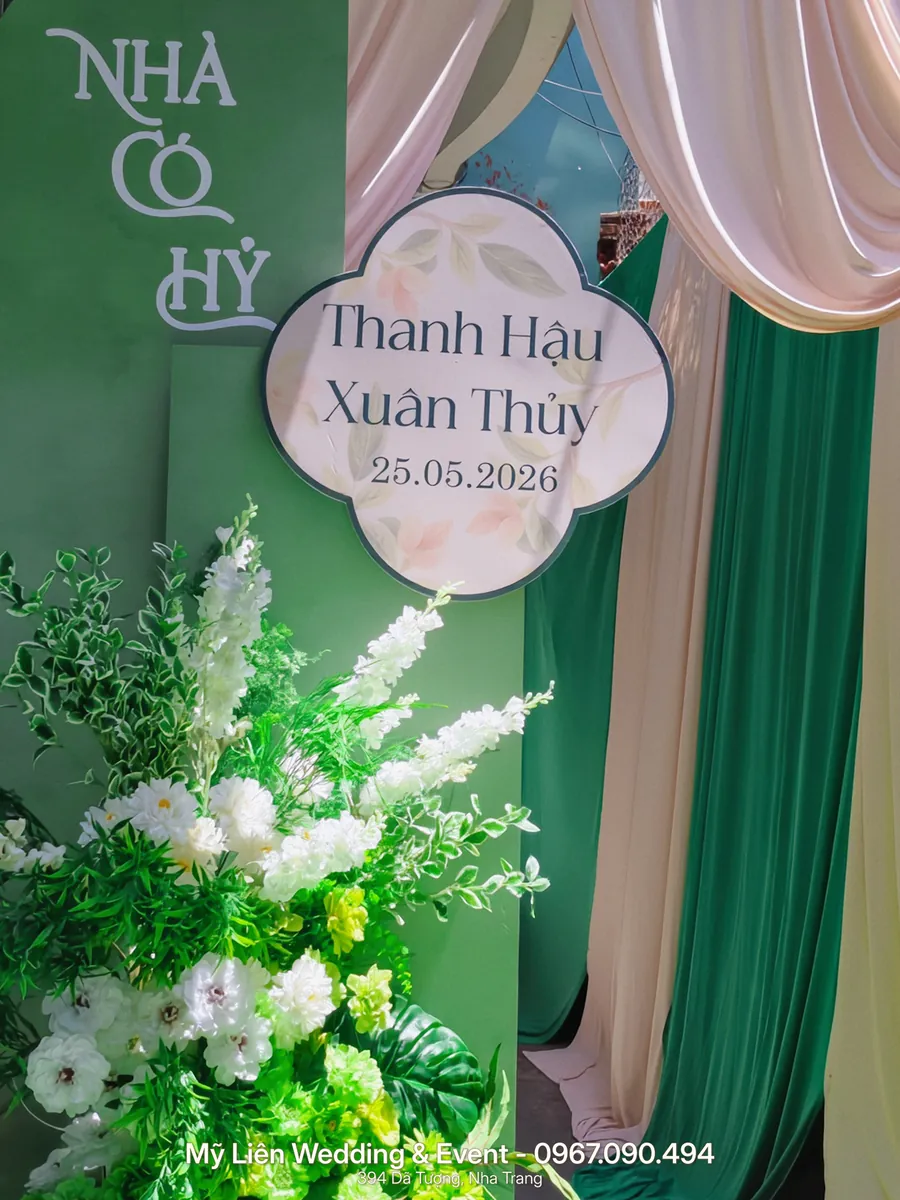 Bảng chào mừng Nhà có hỷ màu xanh lá, rèm kem và cụm hoa lụa trắng, xanh