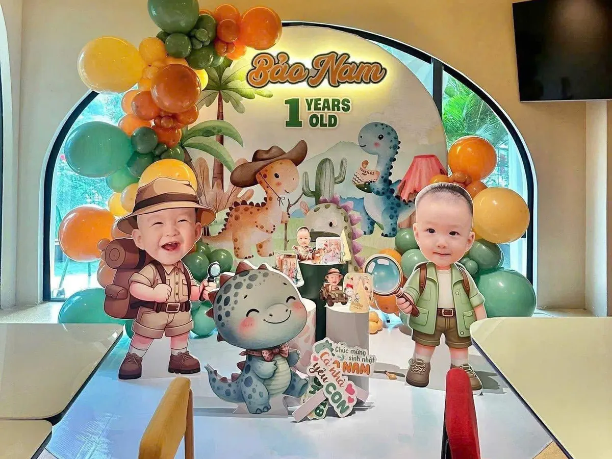 Trang trí thôi nôi chủ đề khủng long thám hiểm với backdrop vòm, bong bóng xanh lá, cam và chibi của bé